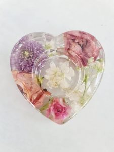 A resin heart shape tealight from birds eye view full of colourful vibrant flowers including a purple dahlia, pink lissianthus and pink spray rose