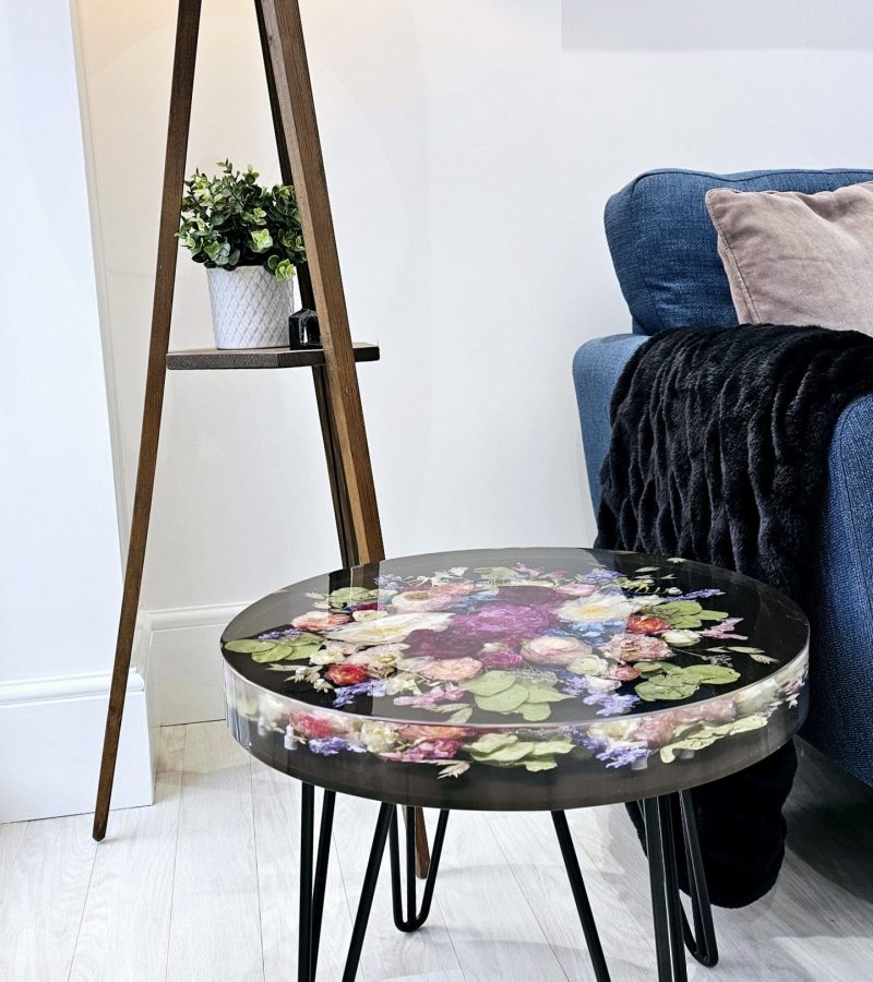 Round resin table with real preserved wedding flowers and black hairpin legs in a modern living room setting.